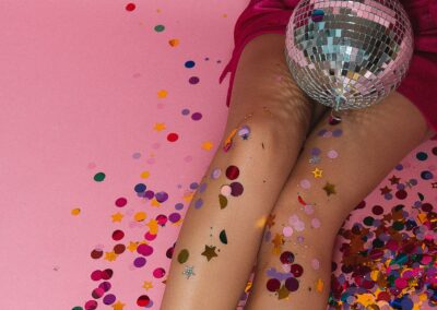 A woman sitting in confetti with a disco ball sitting in her lap.